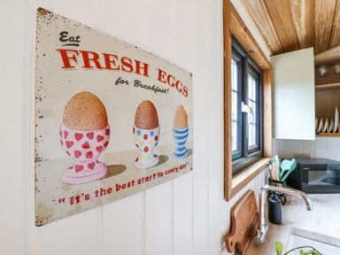 A kitchen wall with a vintage sign about fresh eggs next to a window and a countertop with a faucet and cutting board at Woodpecker Lode near Bottisham