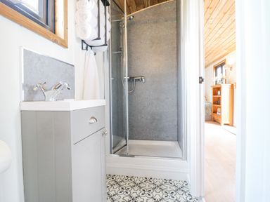 A bathroom with a shower enclosure a sink cabinet and towels with a view into a bedroom at Woodpecker in Lode near Bottisham