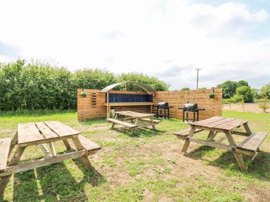 An outdoor area with wooden picnic tables grills and a wooden fence at Woodpecker in Lode near Bottisham