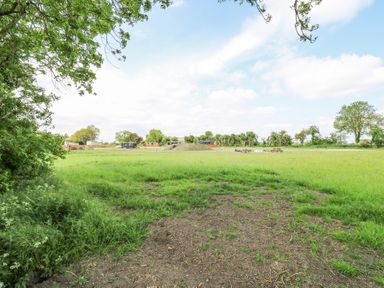 A grassy open field with trees at the edges and some picnic tables in the distance at Woodpecker in Lode near Bottisham