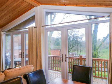 A dining room with sliding doors leading to a wooden deck at Wansfell 2 Limefitt Park near Troutbeck