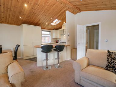 A living room with a kitchen and bar stools at Wansfell 2 Limefitt Park near Troutbeck