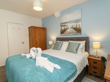 A bedroom with a double bed two bedside tables with lamps a wooden wardrobe and a painting on a blue wall at Old Malthouse Apartment Weymouth