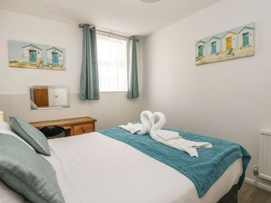 A bedroom with a bed covered with teal bedding and towels folded in swan shapes at Old Malthouse Apartment in Weymouth