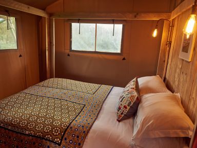A bedroom with a bed covered in patterned bedding and two pillows near two windows at Russet Lodge in Glastonbury