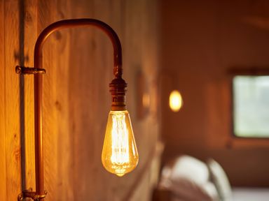 A close-up of a lit vintage light bulb attached to a wall mounted copper pipe in a bedroom at Russet Lodge in Glastonbury
