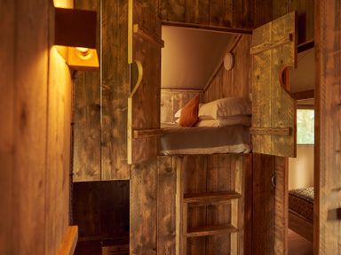 A wooden room with a loft bed accessed by a ladder and heart-shaped cutouts on doors at Russet Lodge in Glastonbury