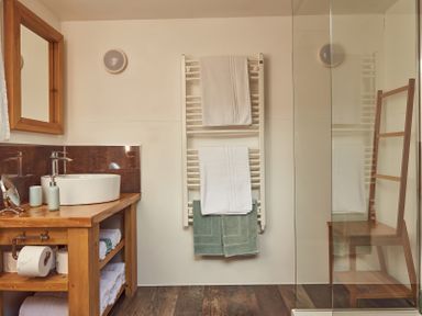 A bathroom with a wooden countertop and mirror a white sink a towel rack with white and green towels and a wooden chair behind a glass shower at Russet Lodge in Glastonbury
