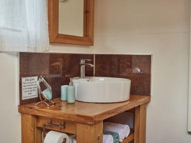 A bathroom sink area with a wooden countertop a round white basin sink a mirror toiletries and folded towels at Russet Lodge in Glastonbury