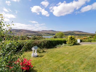 A garden with a small wishing well flowers and bushes with hills and a lake in the background at LOCH ILLION VIEW in Dungloe County Donegal