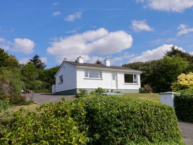A small white house with two chimneys surrounded by a garden and greenery at LOCH ILLION VIEW in Dungloe County Donegal