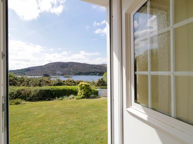 View of a lawn garden hedge and hill across a lake seen through an open door at LOCH ILLION VIEW in Dungloe County Donegal