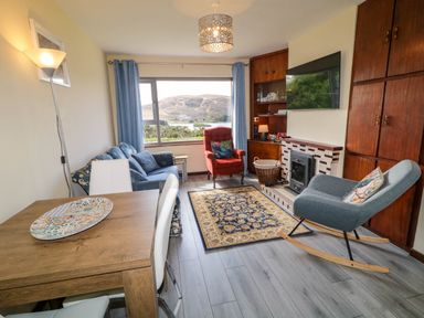 A living room with a wooden dining table white chairs blue sofa red armchair rocking chair and a fireplace at LOCH ILLION VIEW in Dungloe County Donegal