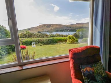 A room with a red armchair and a window showing a garden and hills at LOCH ILLION VIEW in Dungloe County Donegal