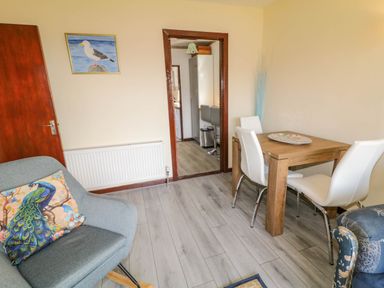 A dining room with a wooden table and white chairs and a gray armchair with a peacock cushion at LOCH ILLION VIEW in Dungloe County Donegal