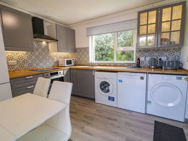 A kitchen with grey cabinets patterned tile backsplash white appliances and a white dining table with chairs at LOCH ILLION VIEW in Dungloe County Donegal