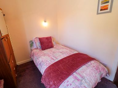 A small bedroom with a single bed covered in patterned bedding and a red throw and cushion at LOCH ILLION VIEW in Dungloe County Donegal