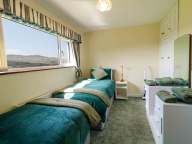 A bedroom with a single bed next to a window showing a mountain view and white furniture including a dresser with mirror at LOCH ILLION VIEW in Dungloe County Donegal