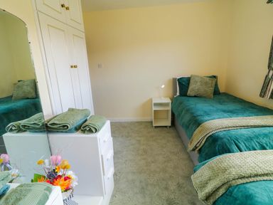 A bedroom with a single bed green bedding a white nightstand with a lamp a white wardrobe and a chest of drawers with towels and flowers at LOCH ILLION VIEW in Dungloe County Donegal