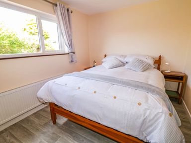 A bedroom with a double bed next to a window with curtains and a small wooden bedside table at LOCH ILLION VIEW in Dungloe County Donegal
