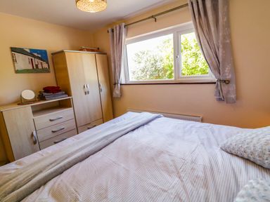 A bedroom with a bed a wooden wardrobe a dresser with towels and a mirror and a window with curtains at LOCH ILLION VIEW in Dungloe County Donegal