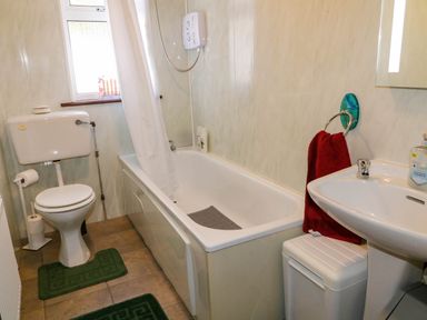 A bathroom with a toilet, bathtub with shower and curtain, sink with a red towel, and a small window at LOCH ILLION VIEW in Dungloe County Donegal