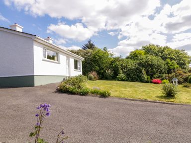A white house with green trim next to a garden with grass shrubs and flowers at LOCH ILLION VIEW in Dungloe County Donegal