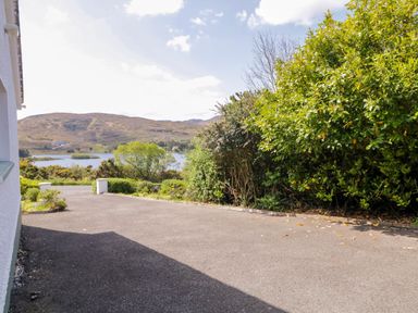 A paved driveway next to bushes and trees with hills and a lake in the background at LOCH ILLION VIEW in Dungloe County Donegal