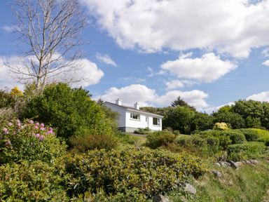 A white house surrounded by trees bushes and flowers under a partly cloudy sky at LOCH ILLION VIEW in Dungloe County Donegal