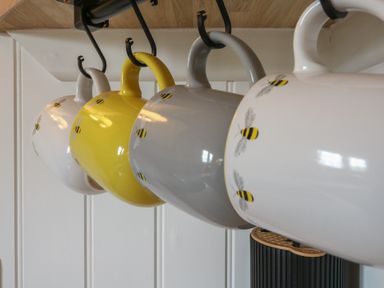 Four ceramic mugs with bee patterns hanging on hooks in a kitchen at The Heron in Lode near Bottisham