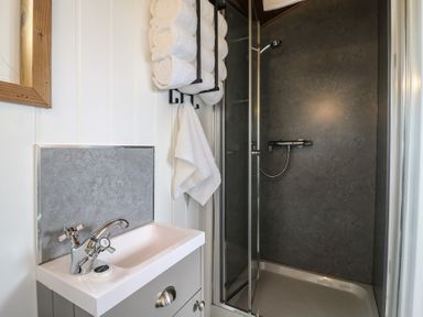 A bathroom with a small sink and faucet towels hanging on a rack next to a shower with glass doors and a dark wall at The Heron in Lode near Bottisham