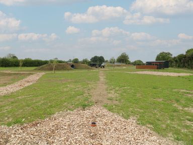 An outdoor area with grass paths wooden chip walkways a grassy mound with a tunnel and small buildings at The Heron in Lode near Bottisham