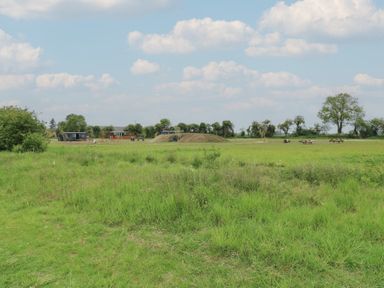 A grassy open field with playground equipment and picnic tables under a cloudy sky at The Heron in Lode near Bottisham