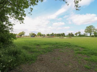 A grassy field with picnic tables and small buildings in the distance at The Heron in Lode near Bottisham