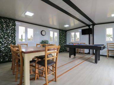 A room with a wooden table and chairs a pool table a wall clock and a television at Barn Owl in Lode near Bottisham