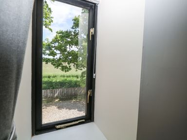 A window showing a view of trees and grass at Lakeside Barn Aylsham
