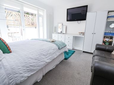 A bedroom with a bed and white bedding a wall-mounted TV a white dresser a white wardrobe and a black armchair at 67 Pendre Avenue in Prestatyn