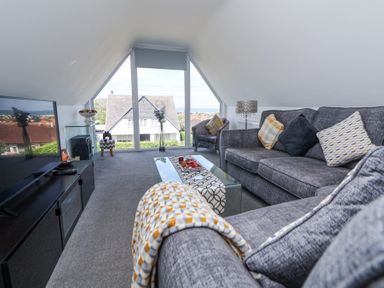 A living room with grey sofas glass coffee table and large window showing house outside at 67 Pendre Avenue in Prestatyn