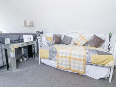 A room with a white daybed with cushions and a yellow patterned blanket next to a mirrored console table with a lamp and telescope at 67 Pendre Avenue in Prestatyn