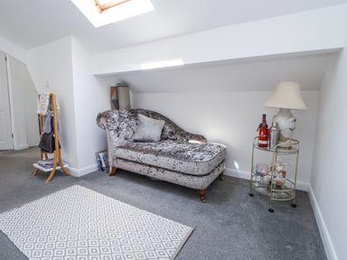A room with a chaise lounge pillow and a small table with a lamp and bottles at 67 Pendre Avenue in Prestatyn