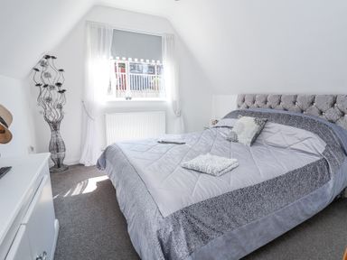 A bedroom with a large bed with folded towels on it a window with curtains a decorative vase and a small cabinet at 67 Pendre Avenue in Prestatyn
