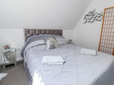 A bedroom with a bed covered in gray bedding two towels on the bed mirrored bedside tables family photos and wall art at 67 Pendre Avenue in Prestatyn