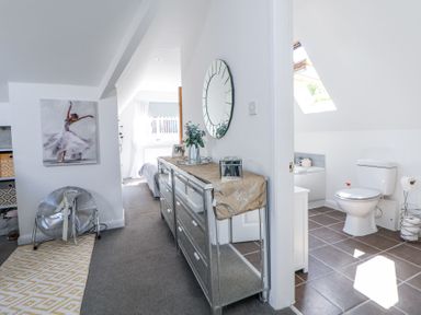 A hallway with a mirrored dresser and a round mirror next to a bathroom with a toilet and a bathtub at 67 Pendre Avenue in Prestatyn