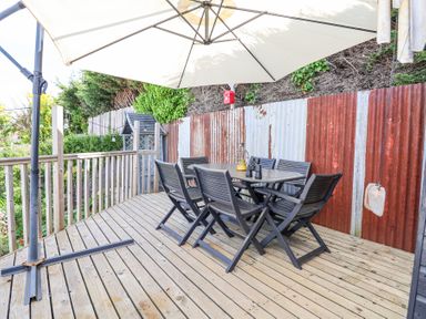 An outdoor wooden deck with a black dining table and six chairs under a large white umbrella at 67 Pendre Avenue in Prestatyn