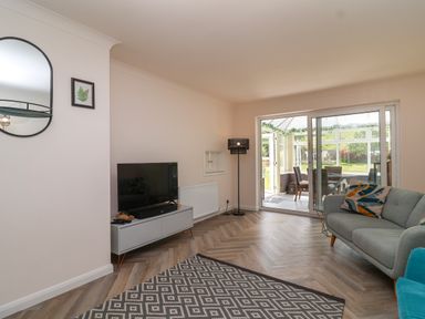 A living room with a TV on a stand a patterned rug a sofa with cushions sliding doors to a conservatory at Hillside in Bishops Cleeve