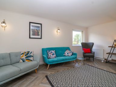 A living room with two sofas a patterned rug a window and wall lights at Hillside in Bishops Cleeve