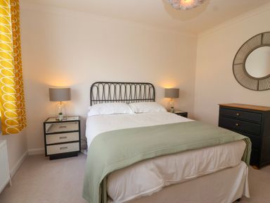 A bedroom with a bed between two bedside tables with lamps a chest of drawers and a round mirror at Hillside in Bishops Cleeve