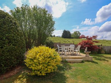 An outdoor patio area with plastic chairs and table surrounded by bushes and grass at Hillside in Bishops Cleeve