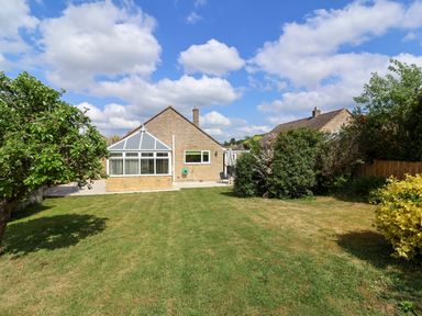 A backyard with a lawn, trees, bushes, and a house with a conservatory at Hillside in Bishops Cleeve