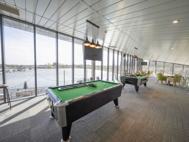 A gaming area with tables for pool and foosball by large windows overlooking water at Starlight Skylight - Billing Aquadrome in Billing Aquadrome Holiday Park